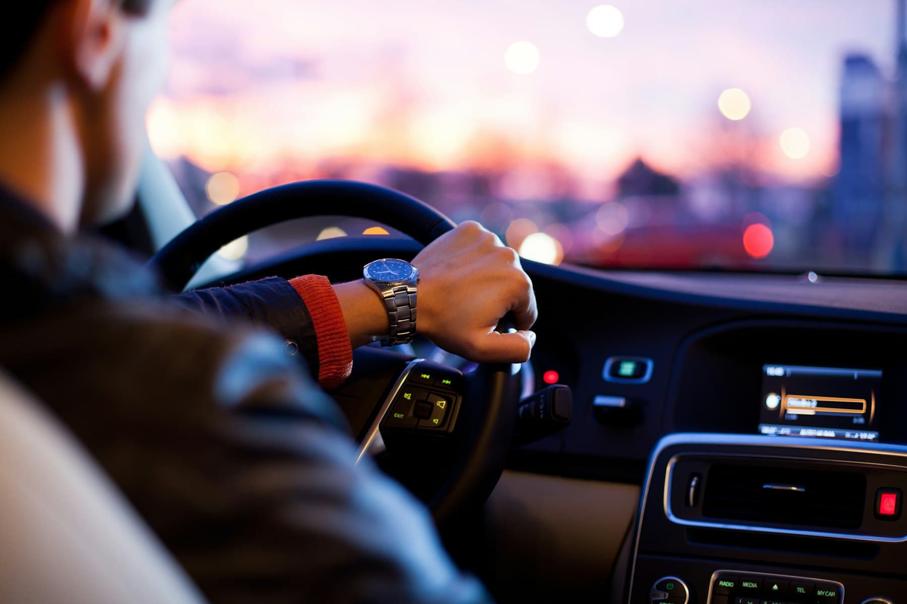 Chauffeur au volant d'une berline, ville éclairée en fin de journée